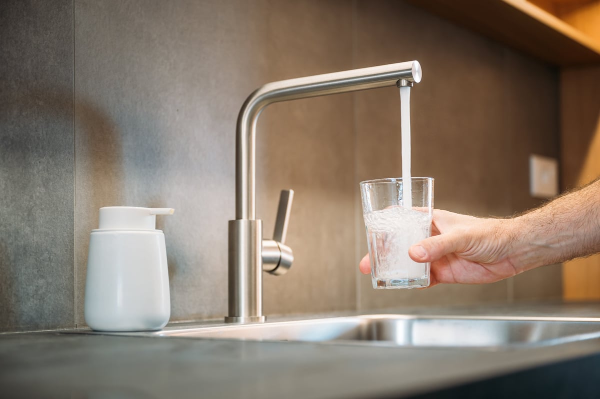 Persona llenando un vaso de agua desde la llave de una cocina moderna y luminosa