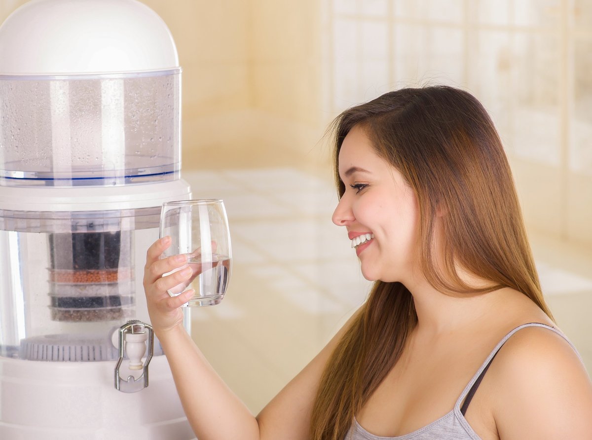 Woman filling glass of water from tabletop water dispenser
