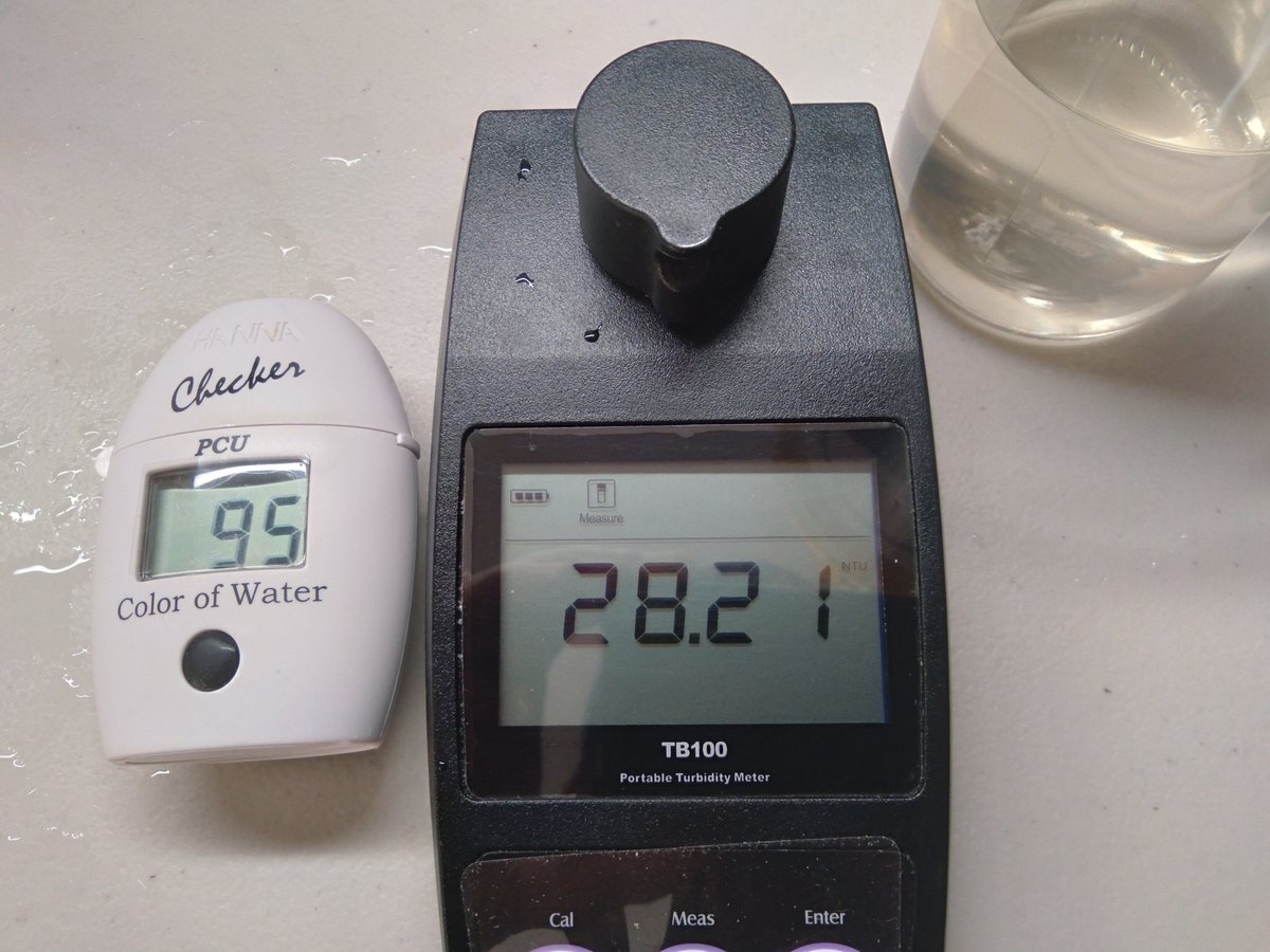 Two water testing devices on a white surface: a white handheld Checker PCU meter showing 95, and a dark TB100 meter displaying 28.2