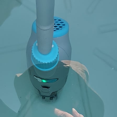 Overhead view of a robotic pool cleaner with blue brushes and dark housing in clear pool water