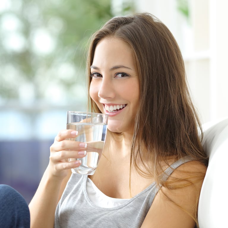 Woman smiling and holding a glass of water indoors with a blurred green background