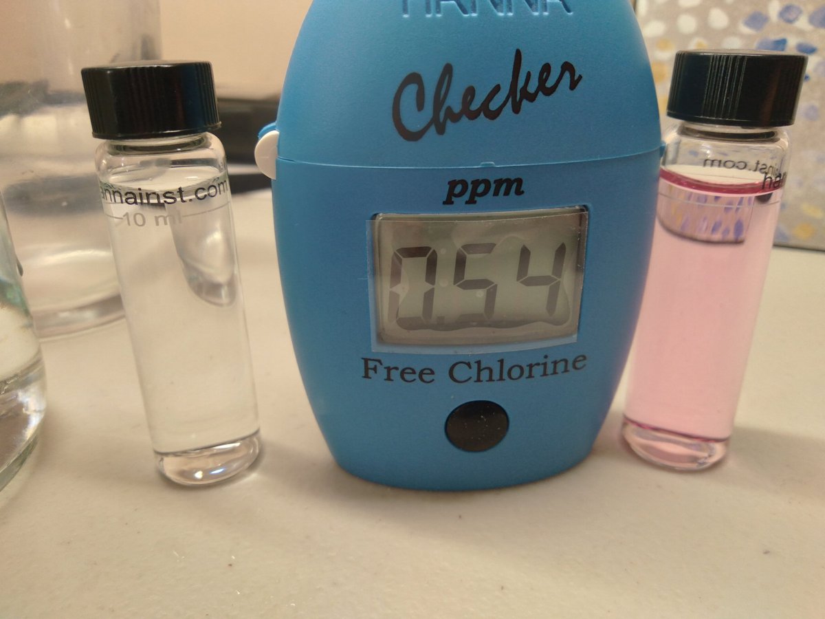 Blue water quality tester showing 95.4 ppm free chlorine reading, flanked by two clear glass vials with black caps