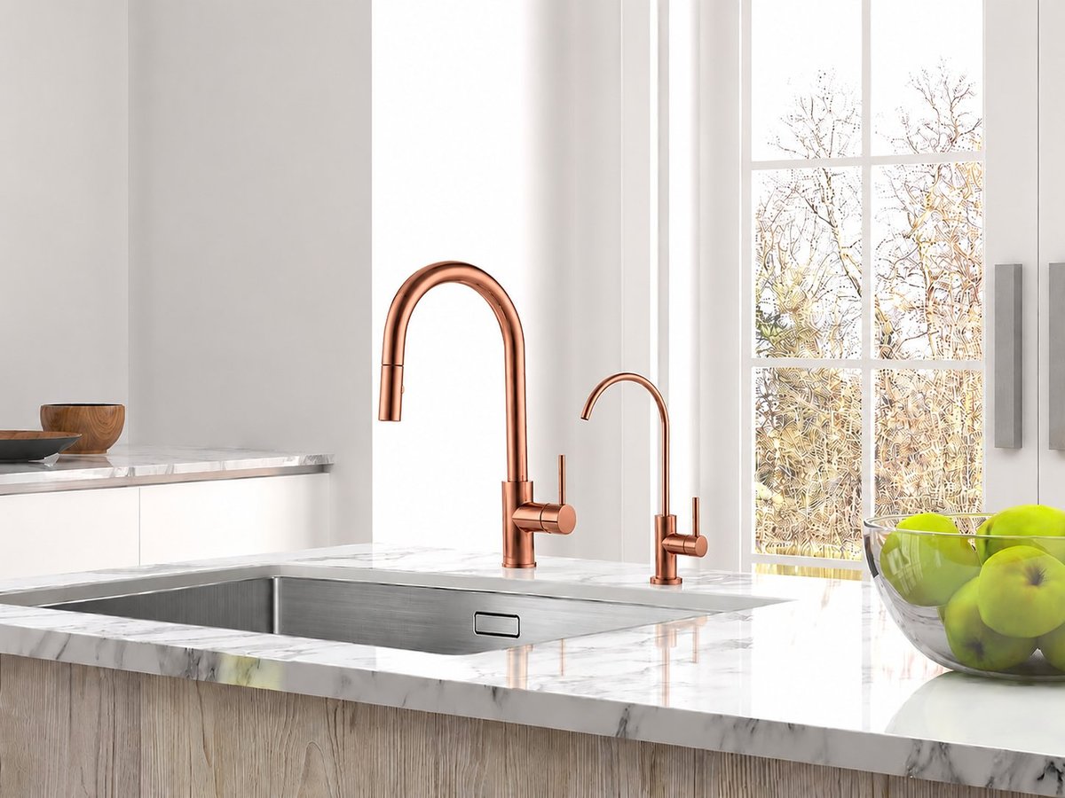 Modern kitchen sink with copper faucets, marble countertop, and green apples in a bowl by a window overlooking bare trees