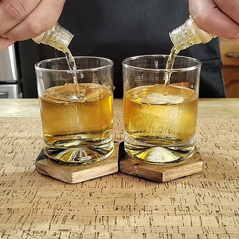 Two glasses of whiskey being poured simultaneously from bottles held in hands, placed on cork coasters