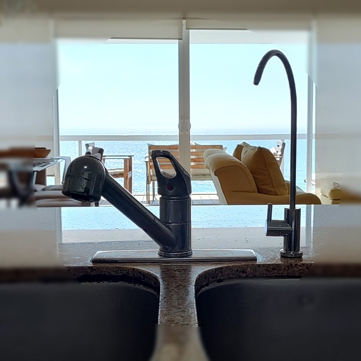 Modern kitchen sink with pull-out faucet and black mixer tap, overlooking large windows with coastal ocean view and lounging chairs on balcony
