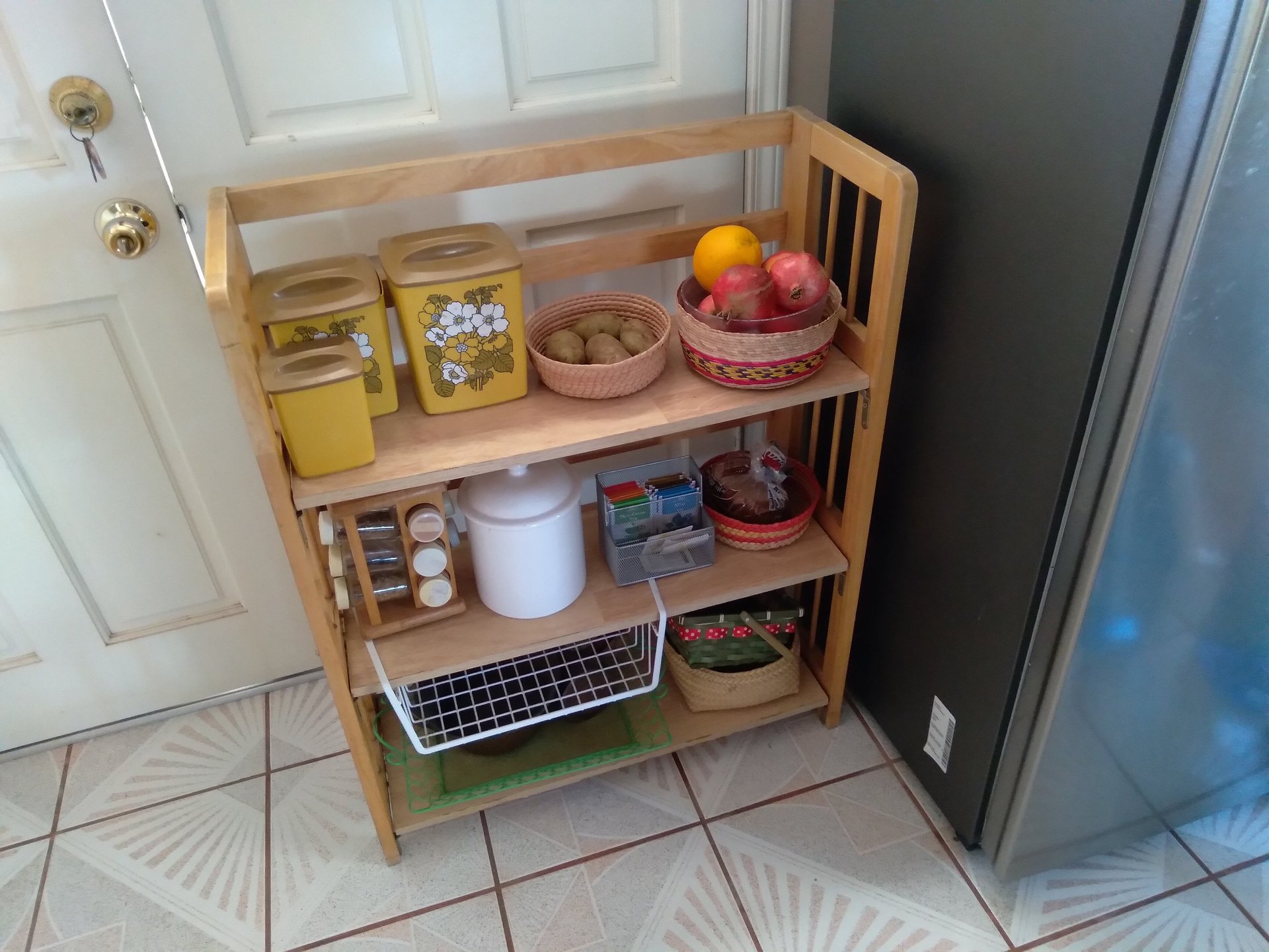 Wooden kitchen shelf unit with organized pantry items including jars, bowls of fresh fruit, and storage containers on multiple tiers