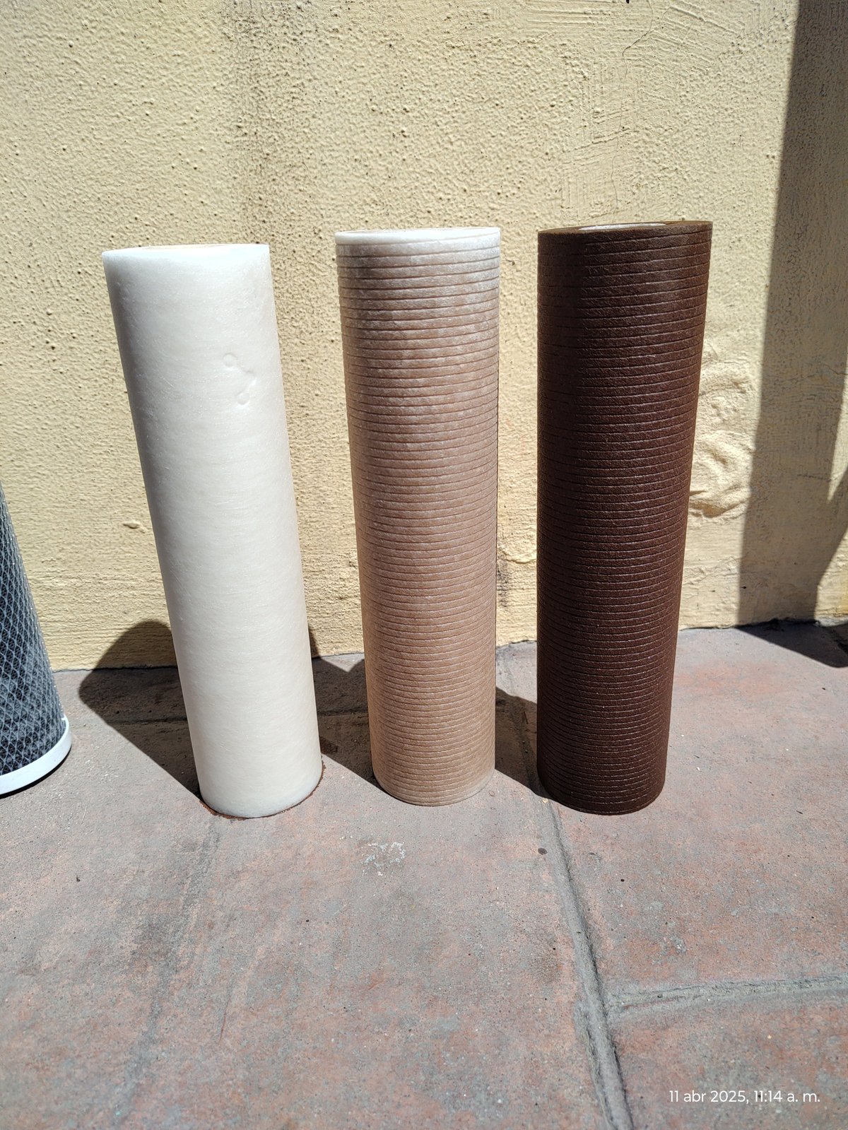 Three cylindrical sisal carpet samples displayed on a patio, showing white, tan, and dark brown colors