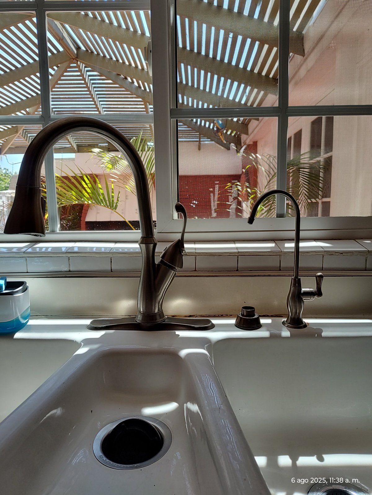 Modern kitchen sink with black pull-down faucet near windows with louvered shades and outdoor views
